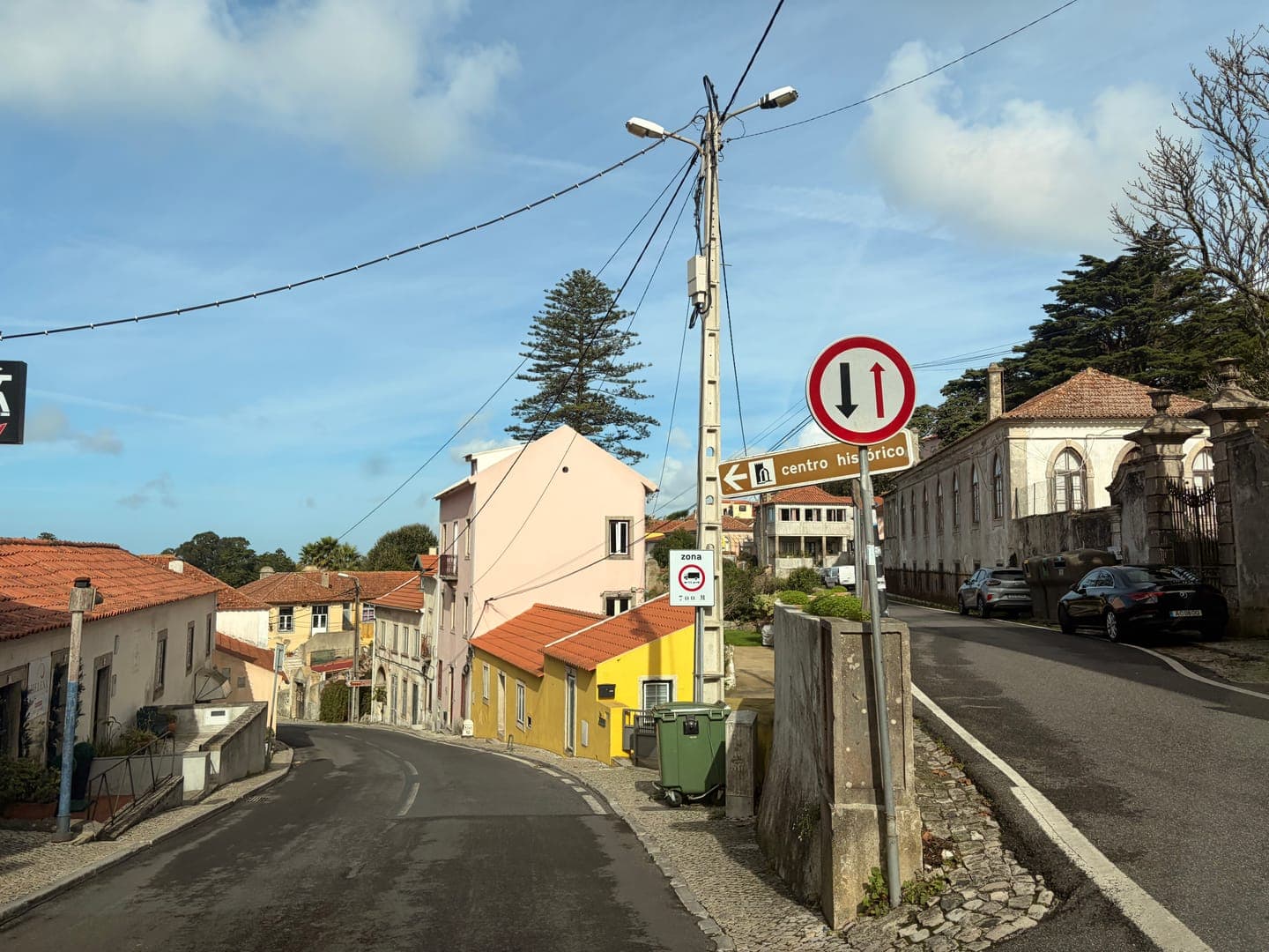This charming street scene captures the essence of a historic Portuguese town, with colorful buildings lining a winding road under a bright blue sky. A prominent sign points the way to 'centro histórico' (historic center), inviting exploration of the area's rich past. The mix of traditional architecture, a clear sky, and the promise of discovery creates a welcoming and picturesque atmosphere.