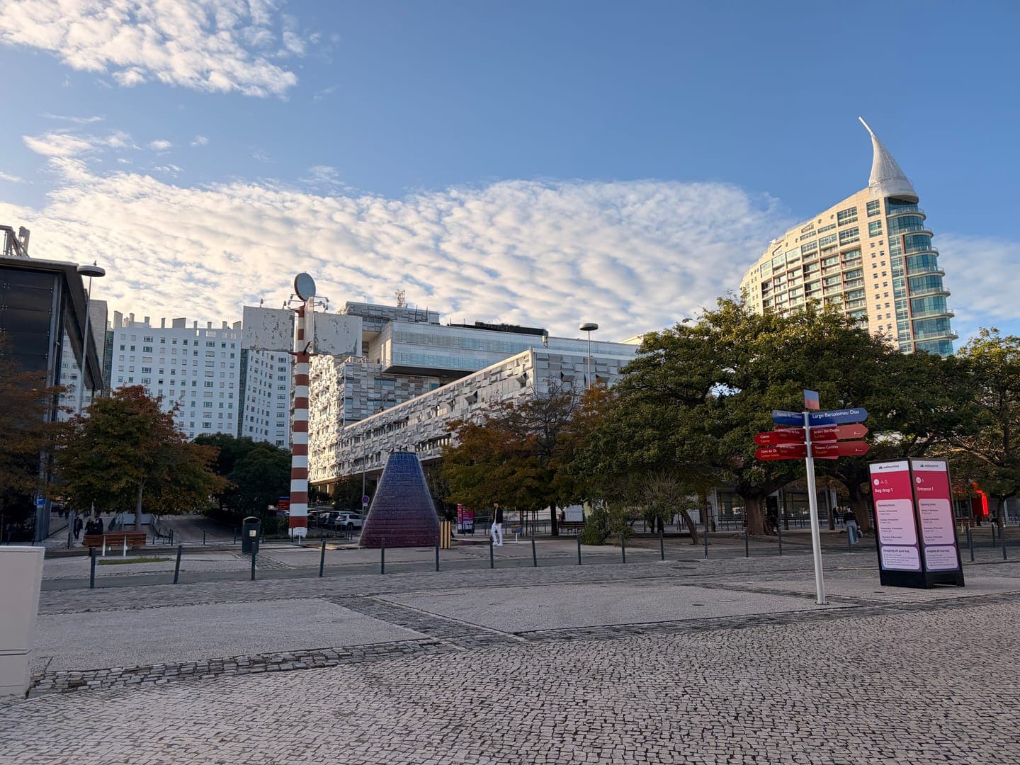 A beautiful day in Lisbon, Portugal, with a clear blue sky and fluffy white clouds overhead. The modern architecture of the city is on full display, with a unique, sail-shaped building standing tall against the skyline. The foreground features a charming cobblestone square, inviting exploration of this vibrant European capital.