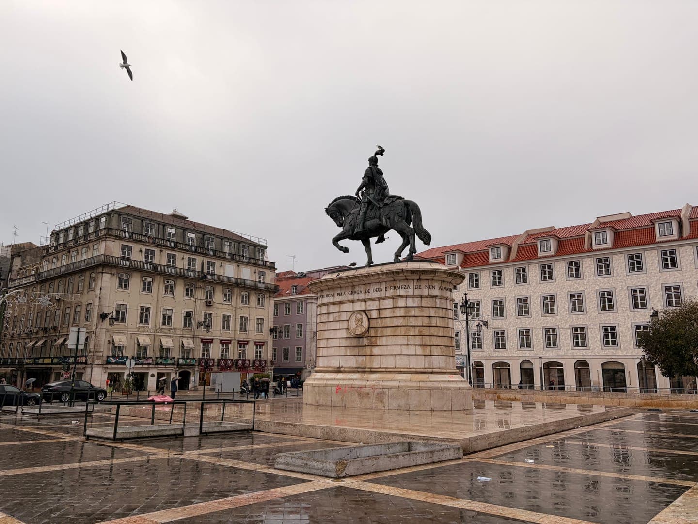 A majestic equestrian statue stands prominently in a historic European square, its dark silhouette contrasting against the overcast sky. The wet cobblestones reflect the surrounding buildings, hinting at recent rain and creating a serene, contemplative atmosphere. A lone bird soars overhead, adding a touch of dynamic movement to the otherwise still scene.
